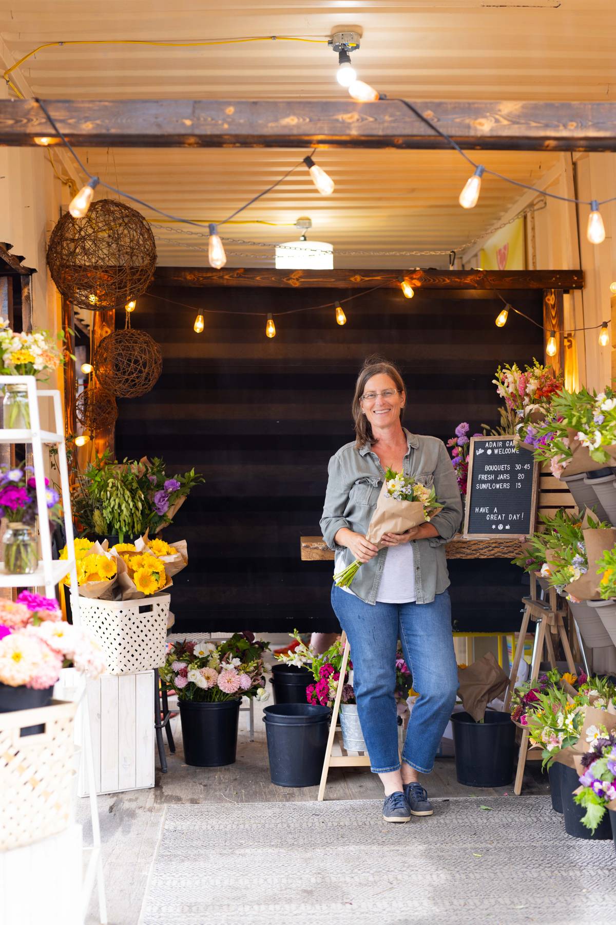 AG Flower Seeds | Owner, Amy, standing in her flower shop holding flowers surrounded by floral arrangements.